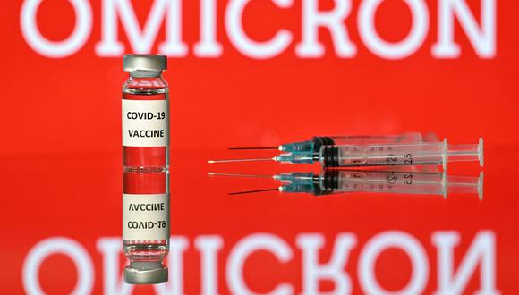 Una imagen de ilustración tomada en Londres el 2 de diciembre de 2021 muestra un vial con la etiqueta vacuna Covid-19 adjunta, junto a las jeringas y una pantalla que muestra la palabra ómicron, el nombre de la nueva variante del coronavirus. (Justin TALLIS / AFP).