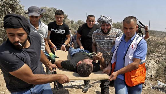 Manifestantes y médicos palestinos evacuan a un joven herido en medio de enfrentamientos con las fuerzas israelíes durante una manifestación contra el puesto de avanzada israelí de Eviatar en la aldea de Beita, al norte de la Cisjordania ocupada, el 6 de agosto de 2021. (Foto: Jaafar Ashtiyeh/ AFP)