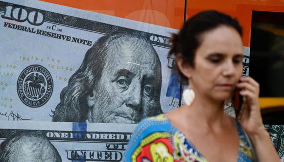 Una mujer pasa junto a una imagen de billetes de dólares estadounidenses en Buenos Aires, Argentina, el 12 de diciembre de 2023. (Foto de Luis ROBAYO/AFP).