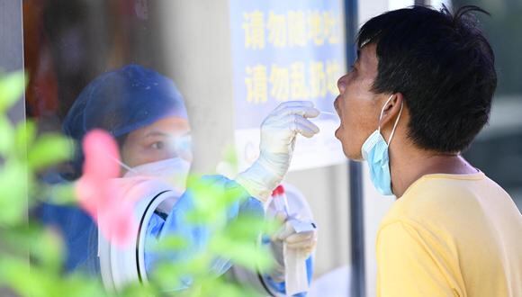 Esta foto tomada el 20 de julio de 2022 muestra a un trabajador de la salud tomando una muestra de hisopo de un hombre para analizarlo por el coronavirus Covid-19 en un sitio de recolección de hisopos en Nanning, en la región sureña de Guangxi en China. (Foto de AFP) / China FUERA