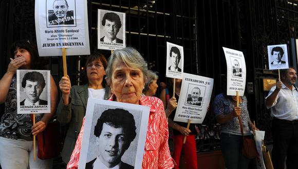 La madre de Hernan Abriata, desaparecido tras ser arrestado en 1976, sostiene la imagen de su hijo junto a un grupo que lleva carteles con la cara del expolicía Mario Sandoval a las afueras de la embajada francesa en Buenos Aires. (AFP)