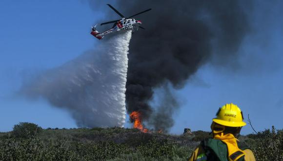 Un bombero observa cómo un helicóptero arroja agua sobre un incendio forestal en Laguna Beach, California después de varias horas, los funcionarios se mostraron optimistas de que el incendio podría detenerse. (Foto: AP/Ringo H. W. Chiu)