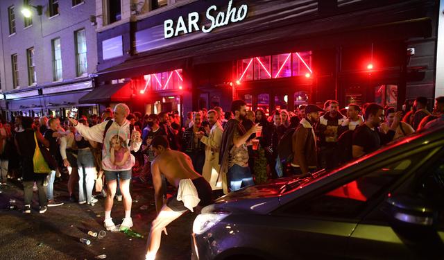 Un automóvil intente avanzar por una calle llena de juerguistas que beben en el área de Soho de Londres. Inglaterra autorizó la reapertura de los pubs que estuvieron cerrados a consecuencia de la pandemia de coronacirus. (Foto por JUSTIN TALLIS / AFP).