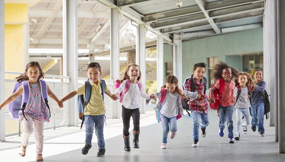 Primary school kids run holding hands in corridor, close up