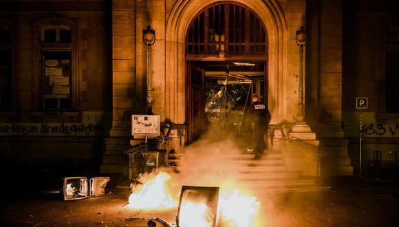 Un oficial de policía intenta extinguir las llamas en la entrada del ayuntamiento del distrito 4 de Lyon, que fue destrozado durante los disturbios que siguieron a una manifestación el 17 de marzo de 2023 en Lyon. (Foto de JEFF PACHOUD / AFP)