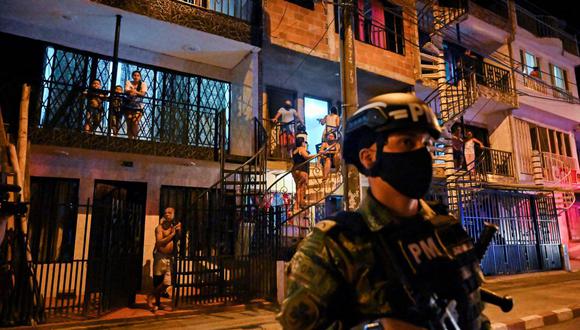 Los residentes miran a los soldados colombianos que custodiaban una calle durante un toque de queda impuesto en los barrios de Cali el 17 de julio de 2020. (Foto de Luis ROBAYO / AFP).