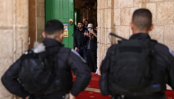 Palestinos se paran dentro de la mezquita de Al Aqsa mientras las fuerzas de seguridad israelíes observan en el complejo en Jerusalén el 9 de abril de 2023. (Foto de AHMAD GHARABLI / AFP)
