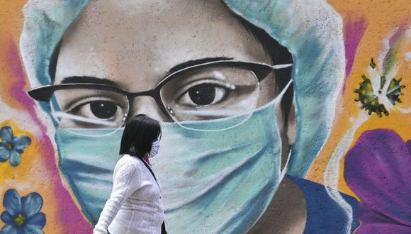 Una mujer pasa junto a un mural relacionado con el coronavirus pintado por el artista urbano Alejandro Bautista Torres, de 38 años, también conocido como Kato, en la Ciudad de México. (Foto: de PEDRO PARDO / AFP).