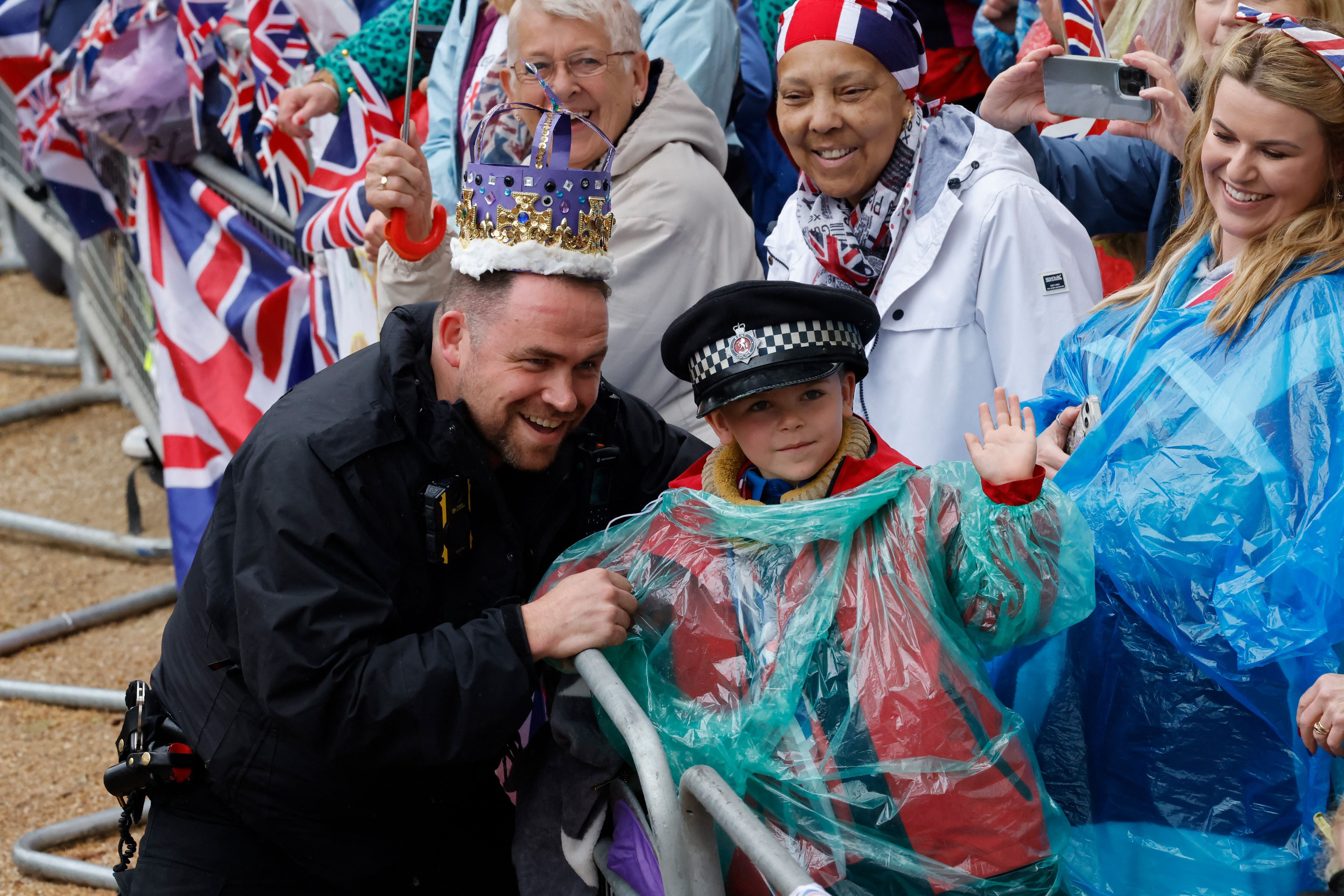 A police officer poses with a young member of the public ahead of the 'King's Procession', a two kilometer stretch from Buckingham Palace to Westminster Abbey, as they await Britain's King Charles III and the Queen Consort Camilla from Great Britain pass into the Diamond State.  (Photo by CARLOS JASSO / AFP)