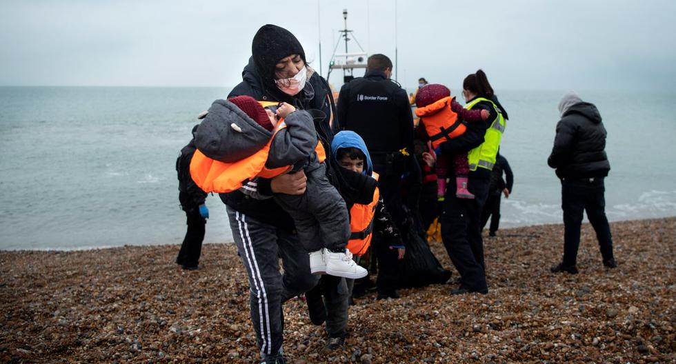 Una migrante lleva a sus hijos tras ser ayudada a desembarcar desde un bote salvavidas en una playa de Dungeness, en la costa sureste de Inglaterra, el 24 de noviembre de 2021, tras ser rescatada mientras cruzaba el Canal de la Mancha. (BEN STANSALL / AFP).