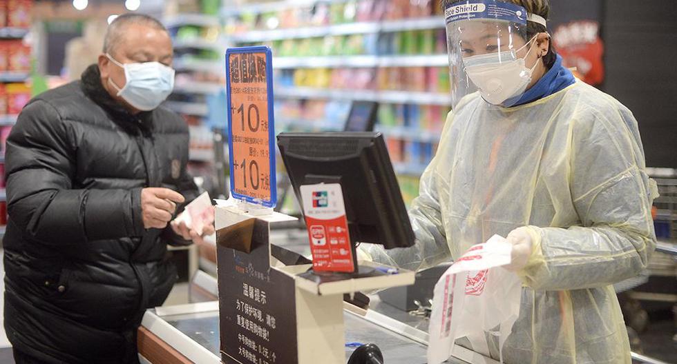 Un cajero trabaja en la caja de un supermercado con una bata de plástico, en Wuhan. (Foto: EFE)