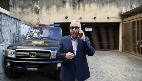 Joel García, abogado del líder de la oposición venezolana Juan Guaidó y de su tío, Juan José Márquez, habla en su teléfono móvil junto al vehículo de contrainteligencia militar fuera de la casa de Márquez, mientras es registrado en Caracas. (Foto: AFP)