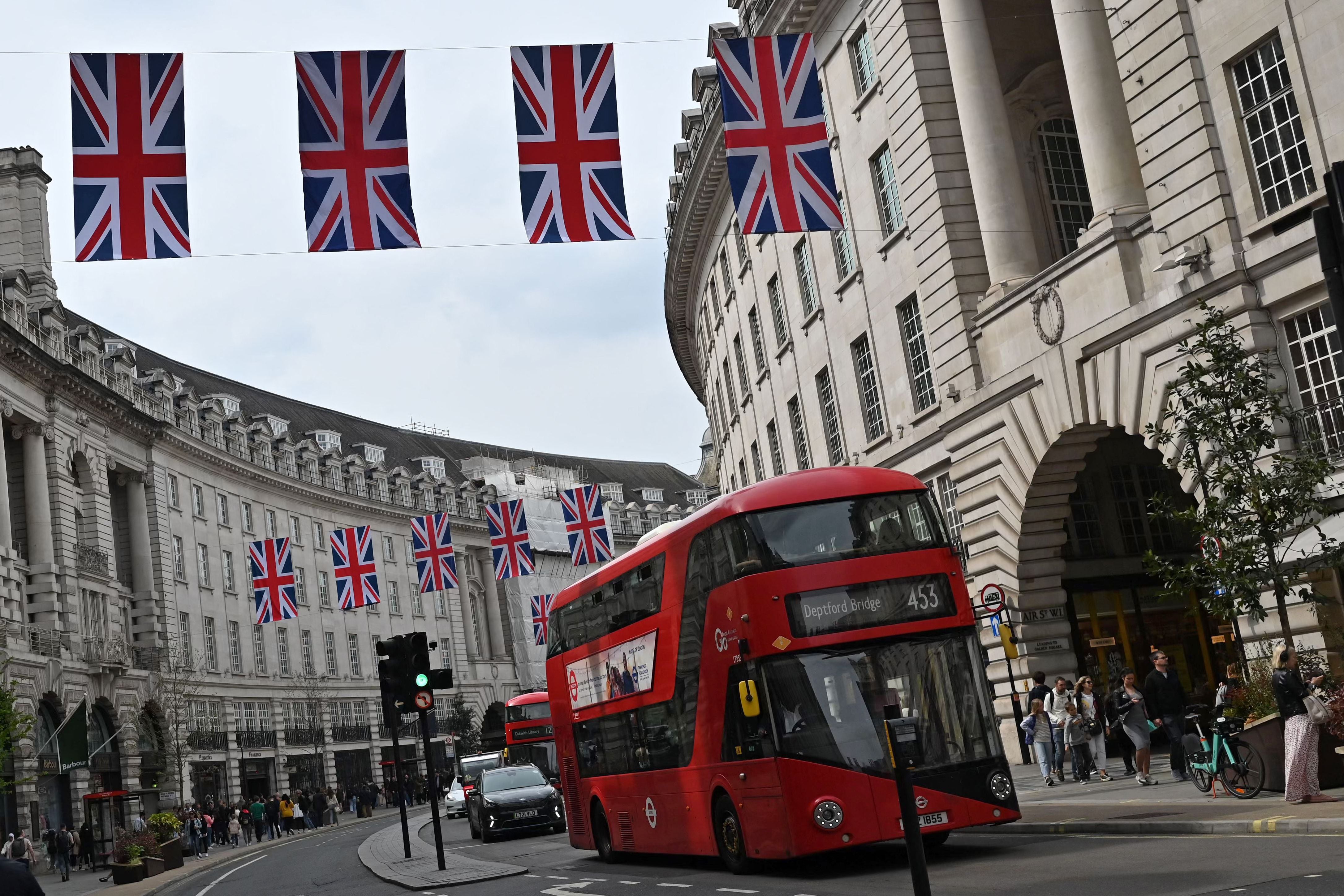 A red London bus passes under the Union Flags in Regent Street in central London on April 30, 2023 ahead of the coronation ceremony for Charles III and his wife, Camilla, as King and Queen of the Kingdom. United.  (Photo by JUSTIN TALLIS / AFP).