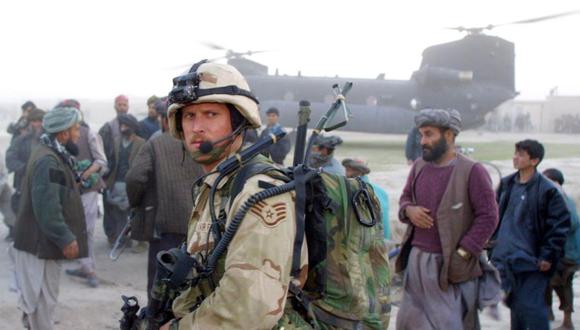 En esta foto de archivo tomada el 15 de noviembre de 2001, un soldado de Operaciones Especiales de la Fuerza Aérea de estados Unidos Hace guardia cerca de un helicóptero Chinook mientras civiles afganos y milicianos leales a la rebelde Alianza del Norte observan en Kwaja Bahuddine. (Foto de BRENNAN LINSLEY / POOL / AFP).