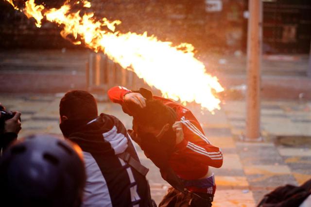 Un hombre se cubre del fuego durante un enfrentamiento con la policía al finalizar una nueva jornada de movilizaciones en el centro de Bogotá, Colombia. (EFE/ Juan Páez).