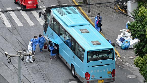 Los residentes con equipo de protección se preparan para abordar un autobús junto a la entrada de un vecindario durante el cierre por coronavirus en Shanghai, China, el 24 de abril de 2022. (Héctor RETAMAL / AFP).