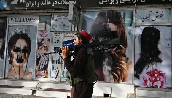 Un combatiente talibán camina frente a una peluquería de Kabul, que muestra fotos publicitarias de mujeres rociadas con pintura negra. Hasta hace unos días, los paneles con imágenes de mujeres eran habituales en la ciudad. (AFP)