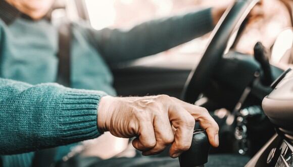 Anciano sosteniendo una mano en el cambio de marchas y la otra en el volante mientras está sentado en su camión. (Imagen: istockphoto / dusanpetkovic)