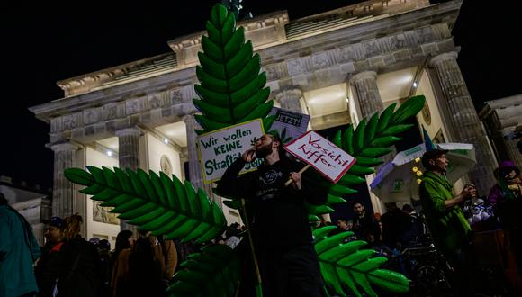 Una persona fuma un porro de marihuana frente a una planta gigante durante una manifestación frente a la Puerta de Brandenburgo de Berlín, en Alemania. (Foto de John MACDOUGALL / AFP).