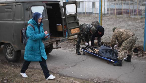 Una mujer camina mientras los militares de Ucrania recogen el cuerpo de un hombre ucraniano que recibió un disparo cuando un vehículo blindado ruso pasó junto a él en el norte de Kiev el 25 de febrero de 2022. (DANIEL LEAL / AFP).