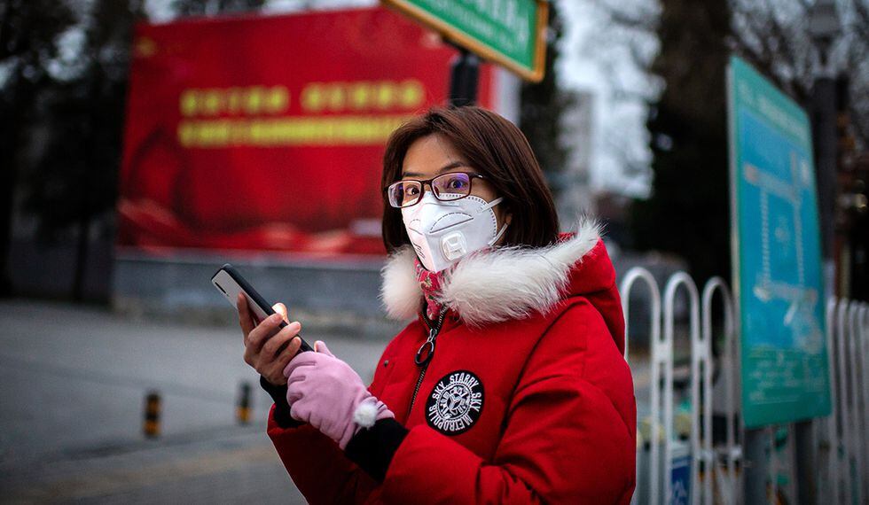 Una mujer con una máscara protectora para protegerse contra el coronavirus COVID-19 navega por su teléfono mientras está parada en una bicicleta (no representada) en una luz roja en una calle en Beijing. (Foto: AFP)