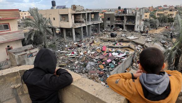 Niños palestinos observan a la gente parada entre los escombros de un edificio destruido durante los ataques israelíes en Rafah, en el sur de la Franja de Gaza, el 20 de noviembre de 2023. (Foto de Mohammed ABED / AFP)