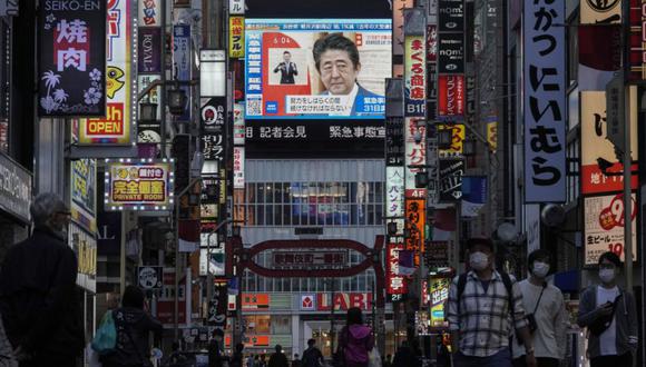 Los peatones pasan frente a una pantalla de televisión pública que muestra al primer ministro japonés, Shinzo Abe, hablando en una conferencia de prensa televisada en Kabukicho, el distrito de entretenimiento más popular y más grande de Shinjuku en Tokio, Japón.
