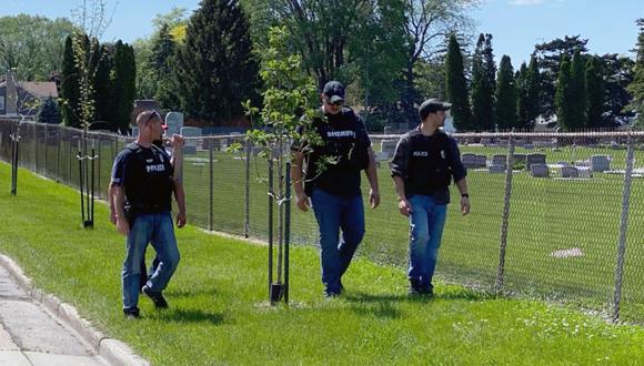 Cuatro agentes de la ley caminan a lo largo de la valla que bordea el cementerio Graceland después de un tiroteo en Racine, Wisconsin.