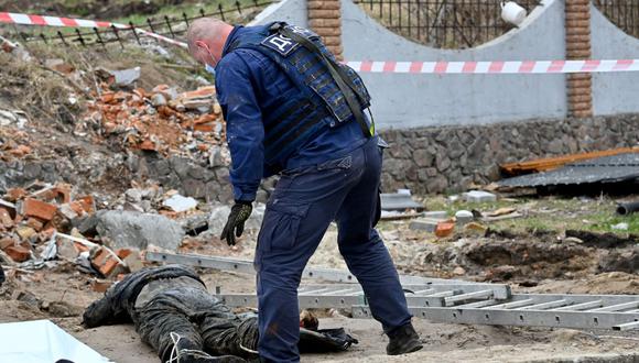 Un rescatista de Ucrania inspecciona un cuerpo descubierto en la alcantarilla de una gasolinera en las afueras de la aldea de Buzova, al oeste de Kiev, el 10 de abril de 2022. (Serguéi SUPINSKY / AFP).