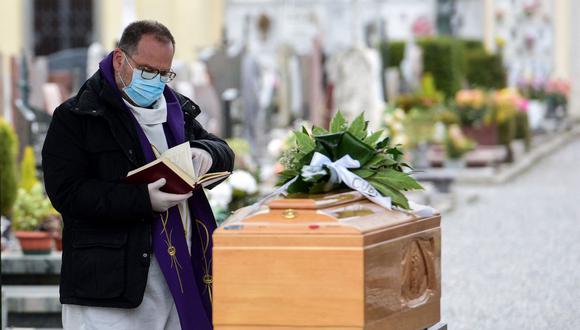 Un sacerdote revisa un libro de ritos funerarios mientras da la última bendición a una persona fallecida en el cementerio de Bolgare, Lombardía, Italia, el 23 de marzo de 2020, en plena pandemia de coronavirus. (Piero CRUCIATTI / AFP).