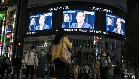 Los peatones caminan por una calle y ven una transmisión de televisión en vivo del primer ministro de Japón, Yoshihide Suga, anunciando el levantamiento del estado de emergencia por coronavirus. (Kazuhiro NOGI / AFP).