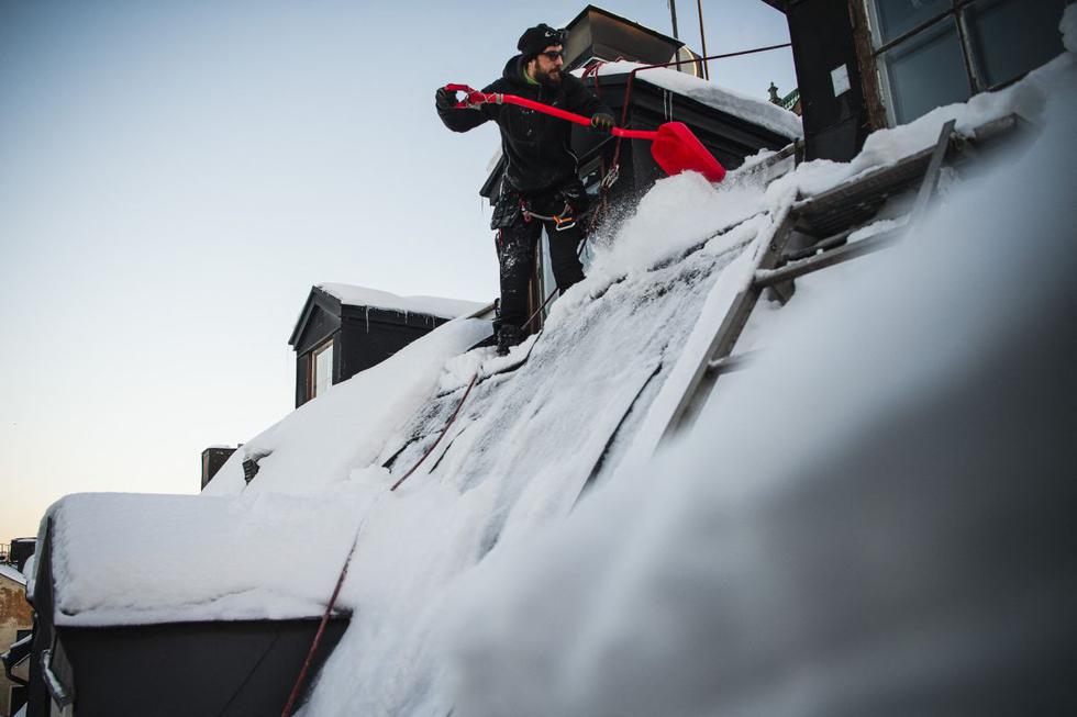 Encaramados a unos diez metros del suelo, Andrei (centro) y Alex quitan el espeso manto blanco que cubre el tejado de un edificio de Estocolmo, mientras su colega se asegura de que no caiga sobre los peatones. (Texto y foto: AFP).