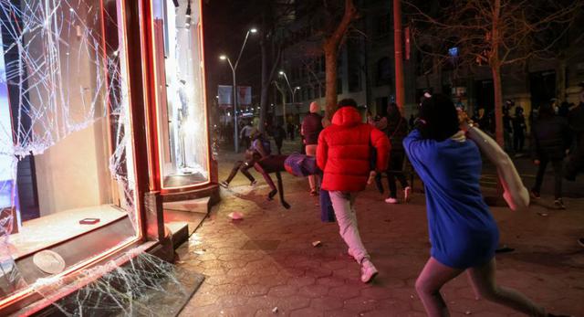 Un manifestante que lleva un objeto corre hacia una ventana dañada de una tienda, mientras los partidarios del rapero catalán arrestado Pablo Hasel protestan en Barcelona, ​​España. (REUTERS / Nacho Doce).