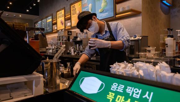 Un barista sirve café como un letrero aconseja a los clientes que usen mascarillas faciales como medida preventiva contra el coronavirus COVID-19 dentro de un café en Seúl el 31 de agosto de 2020. Corea del Sur decidió el 28 de agosto endurecer aún más las restricciones para frenar el rebrote. (Foto: Ed JONES / AFP)