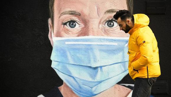 Un joven sin mascarilla camina delante de un mural relativo a la pandemia del coronavirus COVID-19 en Manchester, Inglaterra. (Foto: AFP)