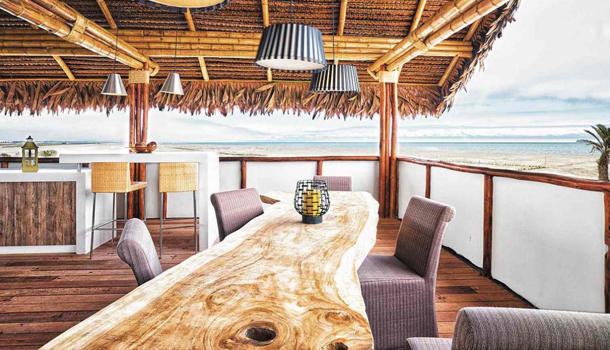 El techo de esta casa de playa está hecho con un entramado de cañas cubiertas con hojas de palma. La mesa de comedor fabricada con un tronco, destaca las vetas naturales, reforzando un concepto rústico. (Foto: Yupana Arquitectos)