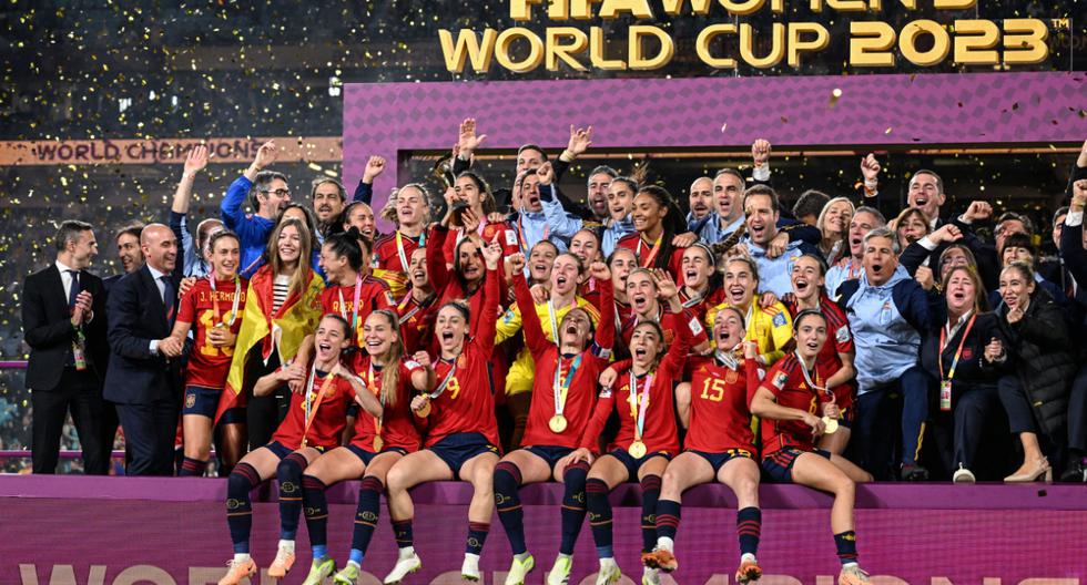 La Reina Letizia (en el centro) de España levanta el trofeo mientras las jugadoras y oficiales de España celebran después de ganar el partido de fútbol final de la Copa Mundial Femenina de Australia y Nueva Zelanda 2023 entre España e Inglaterra en el Estadio Australia en Sídney el 20 de agosto de 2023. | Crédito: WILLIAM WEST / AFP