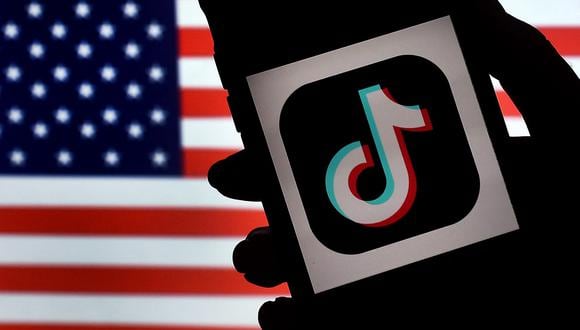 El logotipo de la aplicación de redes sociales, TikTok, se muestra en la pantalla de un iPhone sobre un fondo de bandera de EE. UU. en Arlington, Virginia. (Foto de Olivier DOULIERY / AFP)