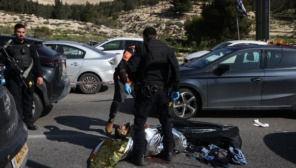 Las fuerzas de seguridad israelíes revisan el cuerpo de un hombre tirado en la carretera en medio de vehículos detenidos en el lugar de un ataque a tiros el 22 de febrero de 2024, cerca del asentamiento de Maale Adumim, al este de Jerusalén. (Foto de AHMAD GHARABLI / AFP)