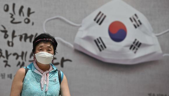Una mujer camina frente a una pancarta que muestra una mascarilla exhibida en la pared del ayuntamiento de Seúl. (Jung Yeon-je / AFP).