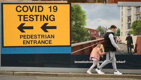 Las personas pasan junto a un letrero que dirige al público a un centro de pruebas de coronavirus Covid-19 en Bolton, noroeste de Inglaterra, el 28 de mayo de 2021. (Foto de Oli SCARFF / AFP).