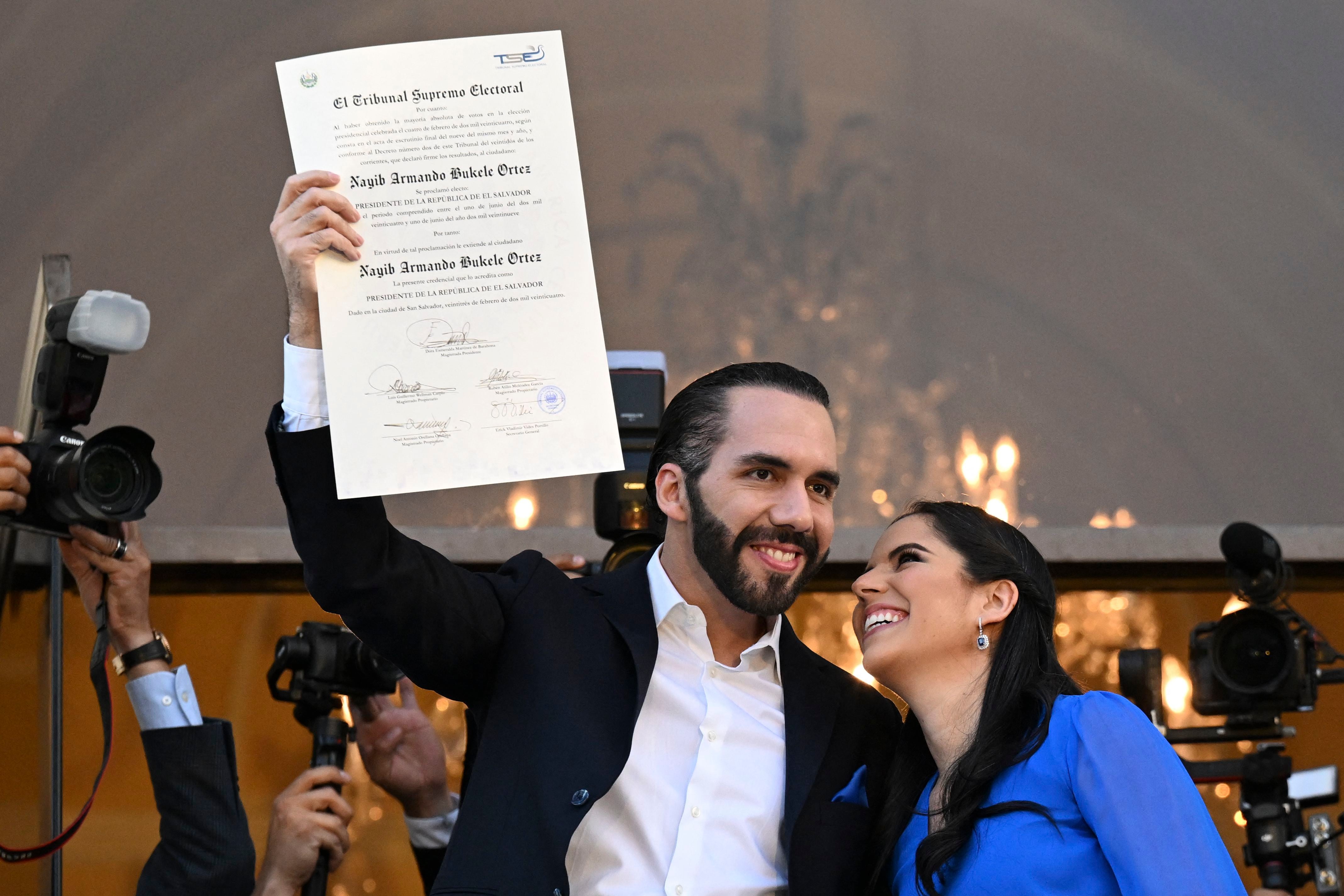 El presidente de El Salvador, Nayib Bukele, acompañado de su esposa Gabriela Rodríguez, muestra la certificación que lo acredita como mandatario electo para el período 2024 2029. (Foto de Marvin RECINOS / AFP).