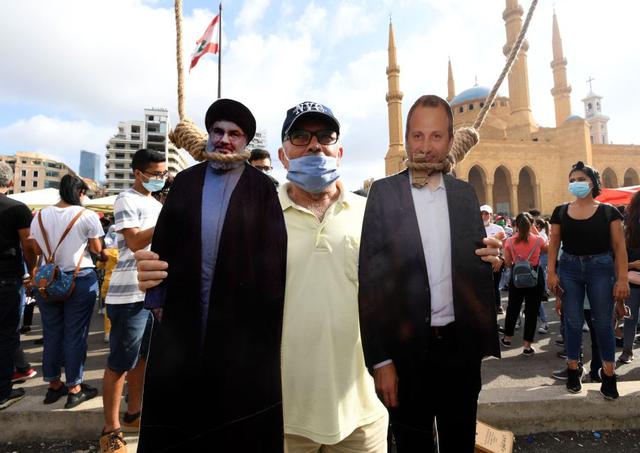 Un hombre posa para una foto con un recorte de cartón de Hassan Nasrallah (izquierda), líder del movimiento musulmán chiita Hezbolá, y el exministro de Relaciones Exteriores Gibran Bassil colgado por manifestantes libaneses en el centro de Beirut. (Foto: AFP).