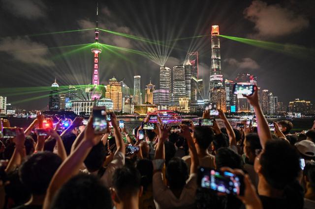 La gente mira un espectáculo de luces en el paseo Bund en Shanghai el 30 de junio de 2021, en vísperas del centenario del Partido Comunista Chino. (Foto de Hector RETAMAL / AFP).