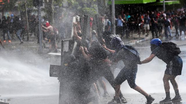 Manifestantes se defienden de chorros de agua lanzados por la policía en Santiago. (Foto: Reuters)