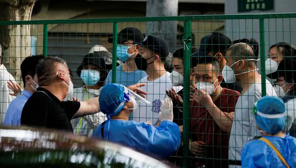 Los residentes que usan máscaras protectoras hablan con el personal de seguridad y los trabajadores con trajes protectores en un área cercada donde existen restricciones para frenar la enfermedad del coronavirus (COVID-19), en Shanghái, China.