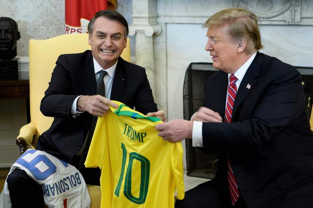 Donald Trump y Jair Bolsonaro intercambiaron las camisetas de las selecciones nacionales de sus países en un inesperado acto que rompió el protocolo y demuestra la buena relación entre las dos economías más grandes de América. (AFP)