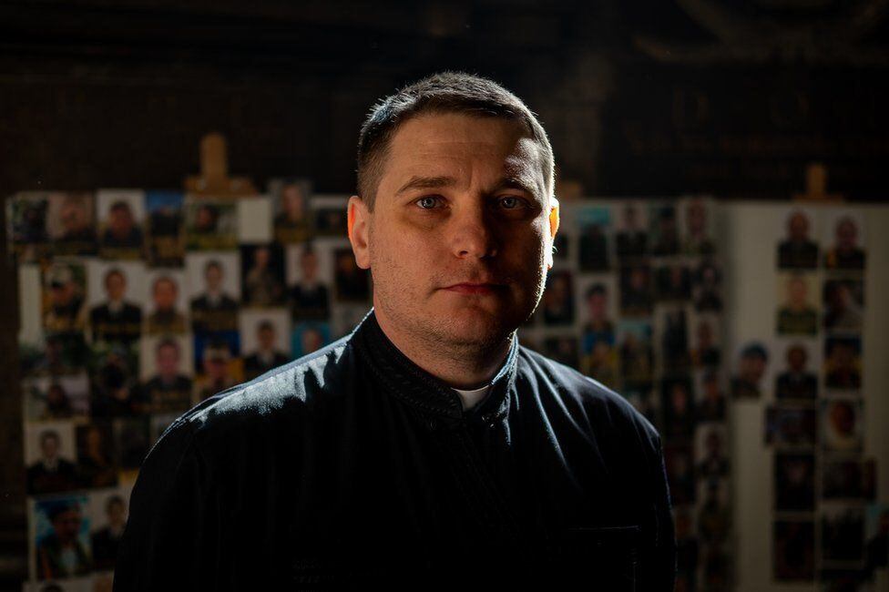 Father Vsevolod stands in front of the portraits of the dead. 