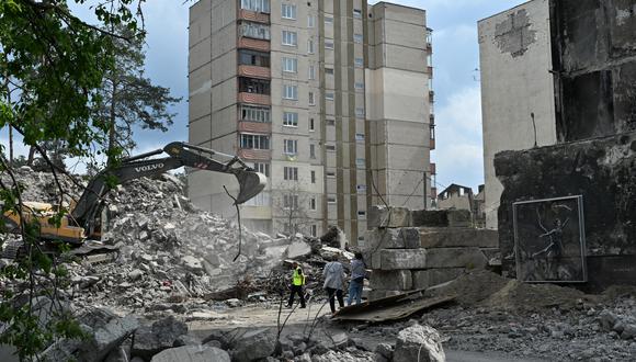 Los trabajadores limpian los escombros de un edificio residencial desmantelado cerca de una obra de arte del artista británico Banksy (derecha), cubierta con un vidrio orgánico protector, en Irpin el 4 de mayo de 2023, en medio de la invasión rusa de Ucrania. (Foto de Genya SAVILOV / AFP)