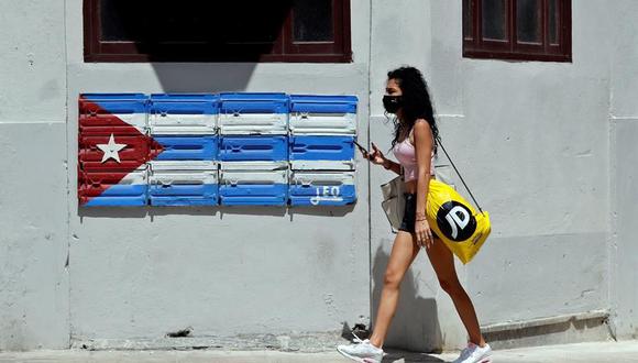 Una mujer con tapabocas camina por una calle que tiene una bandera de Cuba en medio de la pandemia de coronavirus. (Foto: EFE/Ernesto Mastrascusa).